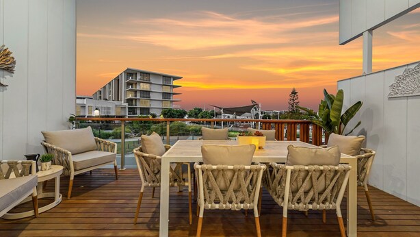 A deck with a table and chairs, overlooking a sunset with buildings in the background.