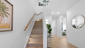 A staircase with wooden steps and a wooden handrail, leading to a room with a bed and a plant.