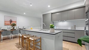 A modern kitchen with a central island, grey cabinets, and a dining area with chairs and a table.