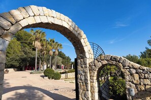 An arched stone gateway leading to a pathway with palm trees and a clear blue sky. - Villa Finca Estel (Calvia)