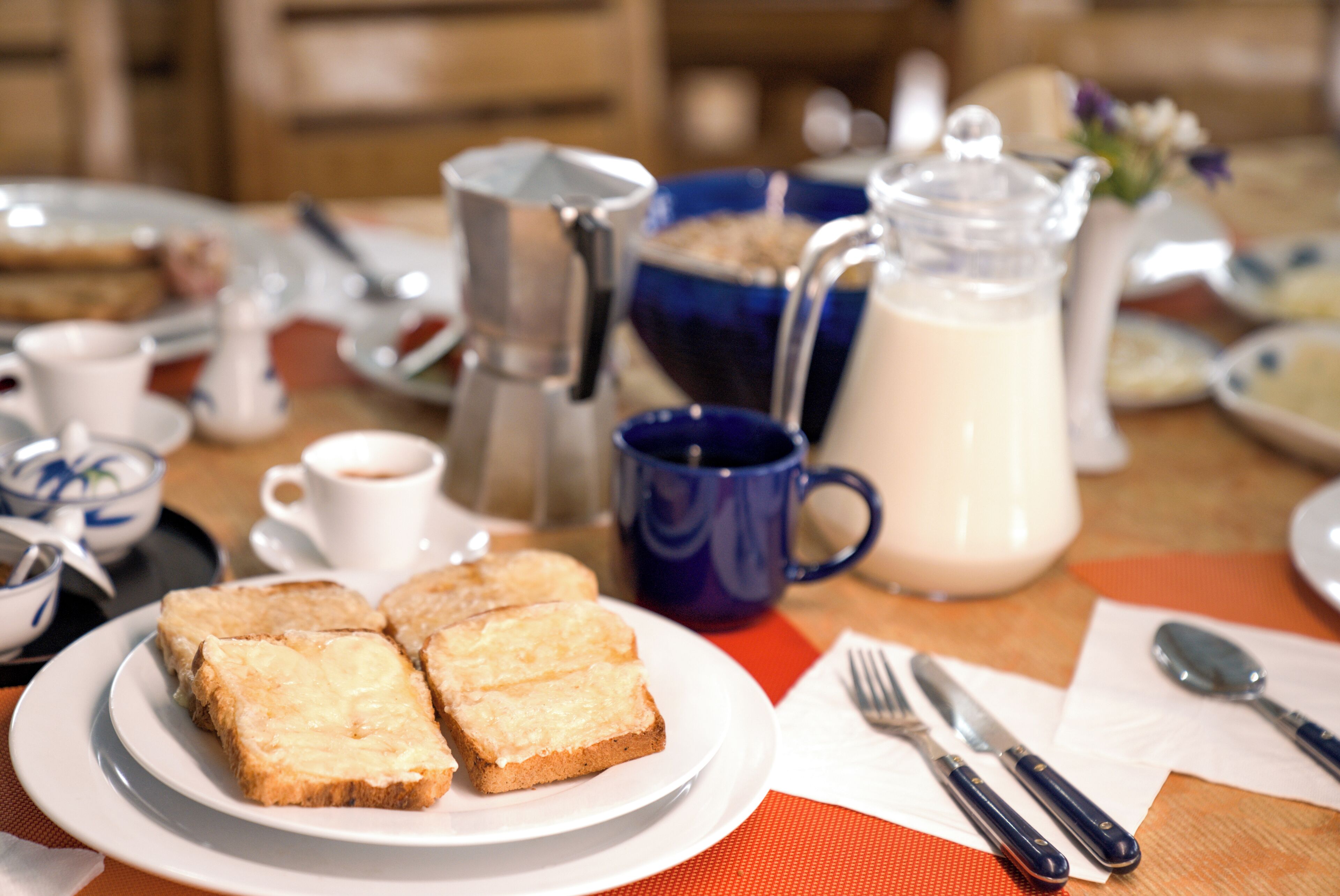 A breakfast setting with toast, coffee, a milk jug, and utensils on a table.