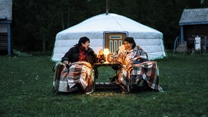 Two people sitting at a table with a lamp in front of a large white tent. - Nature Door Resort. Khuvsgul province. (Alag-Erdene)