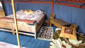 A traditional wooden bed with a colorful bedspread and pillows, a small wooden table, and a chair. - Nature Door Resort. Khuvsgul province. (Alag-Erdene)
