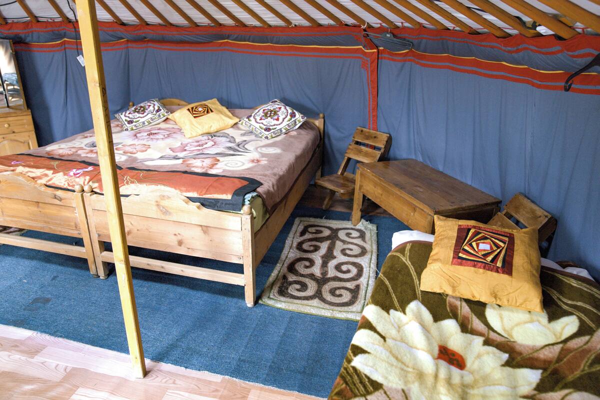Una cama de madera tradicional con una colcha y almohadas coloridas, una pequeña mesa de madera y una silla.