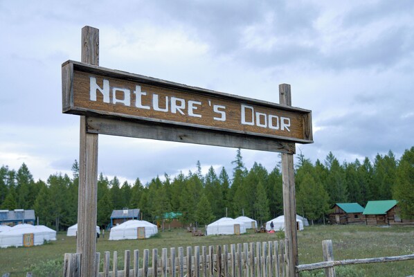 A wooden sign with the text "Nature's Door" in a rustic setting with yurts and a wooden fence. - Nature Door Resort. Khuvsgul province. (Alag-Erdene)