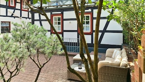 Et traditionelt bindingsværkshus med balkon, en fletsofa og et lille bord med en lygte.