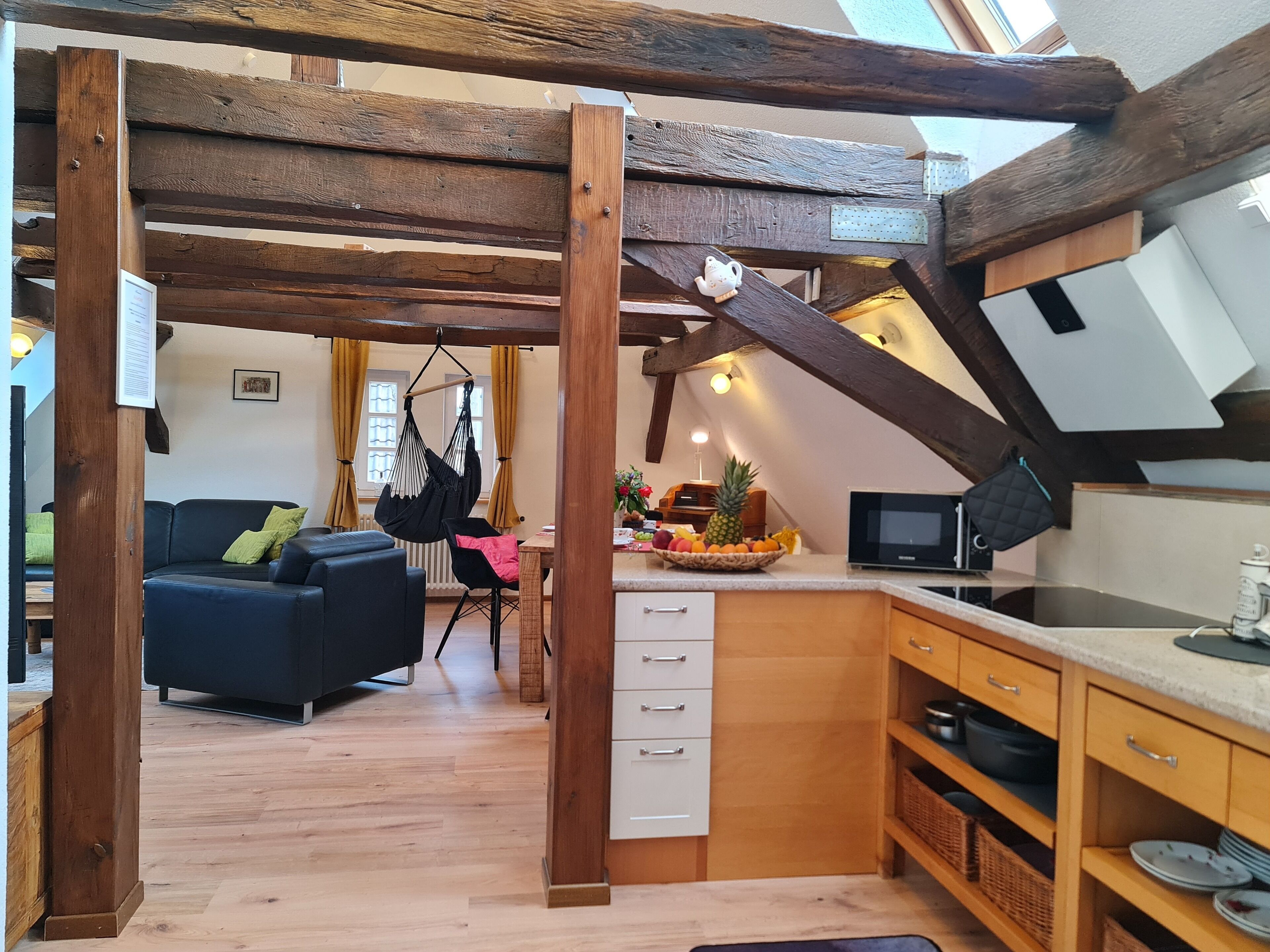 A cozy kitchen with wooden beams, a dining area with a black sofa, and a fruit bowl on the counter.