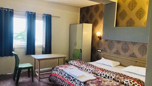 A hotel room with a bed, a desk, a chair, a wardrobe, and a window with curtains. - Sizzling Resort And Adventure (Dhanaulti)