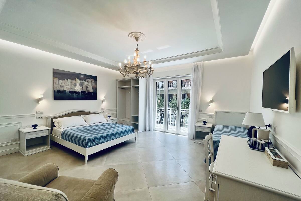 A modern bedroom with a bed, a desk, a chair, a wardrobe, and a balcony with a view.