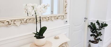 A white ornate console table with a mirror and a potted orchid.