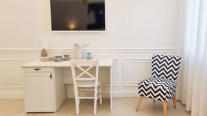 A white desk with a television above it, a white chair, and a black and white patterned chair. - Palazzo Mauro Sorrento Luxury Rooms (Sorrento)