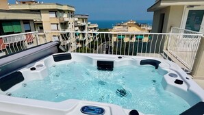 Un jacuzzi sur un balcon offrant une vue sur la mer et les bâtiments environnants.