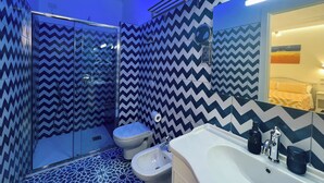 Une salle de bain équipée d’une douche, de toilettes, d’un bidet et d’un lavabo, avec un carrelage au motif en chevron.