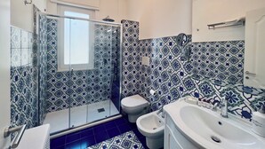 A bathroom with a shower, toilet, bidet, and sink, featuring blue and white patterned tiles. - Palazzo Mauro Sorrento Luxury Rooms (Sorrento)