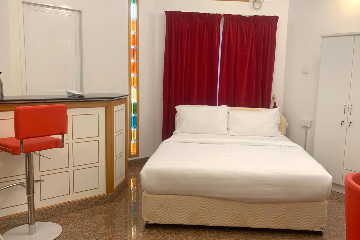 A hotel room with a bed, a desk, a chair, a wardrobe, and a red curtain.