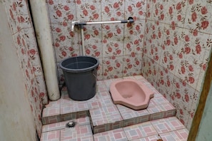 Un baño pequeño con inodoro, un balde y un cabezal de ducha.