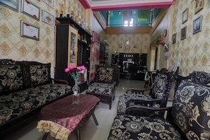 Un salón tradicional con sofás estampados y una mesa de centro, una escalera que conduce a un nivel superior y certificados enmarcados en las paredes.