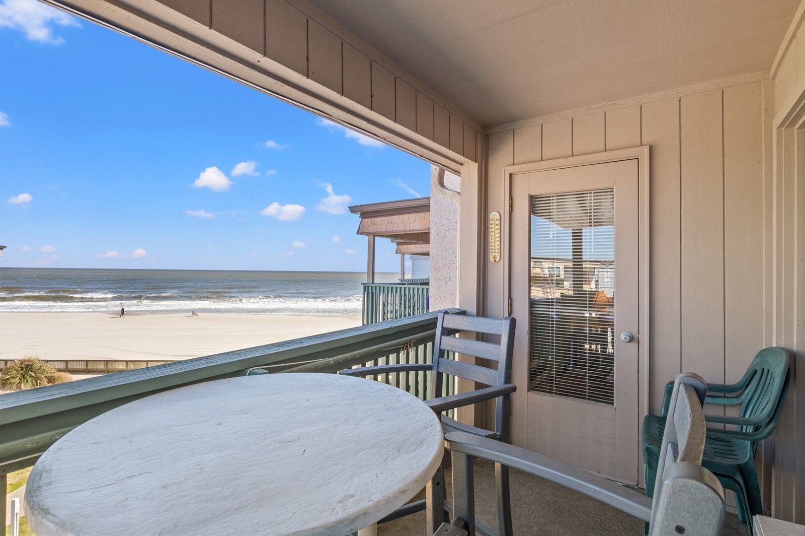 A balcony with a table and chairs, overlooking a beach.