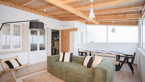 Ein modernes Wohnzimmer mit einem grünen Sofa, Holzbalken an der Decke und einem Essbereich mit Tisch und Stühlen.
