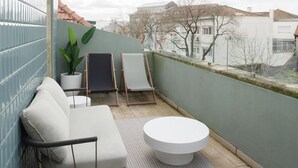 Ein Balkon mit einer weißen Couch, zwei Stühlen, einem kleinen Tisch und einem Blumentopf.