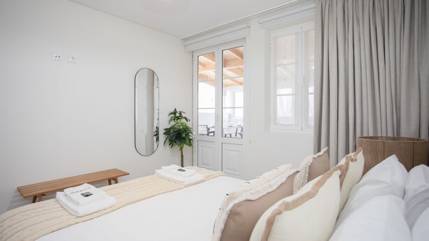Ein Hotelzimmer mit Bett, einer Bank, einem Spiegel, einer Pflanze und Blick ins Freie.