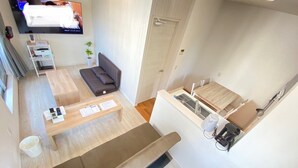 Een moderne, compacte leefruimte met een bank, een eettafel, een kitchenette en een aan de muur bevestigde televisie.