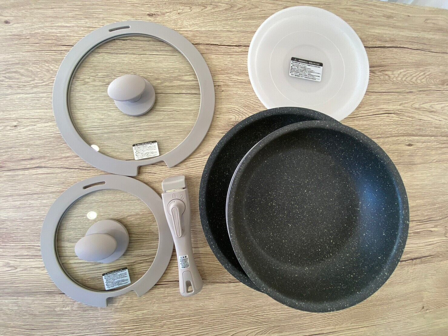 A set of kitchenware including a black frying pan, two grey bowls, and a grey spatula on a wooden surface.