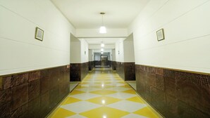 A long, narrow hallway with a checkered yellow and white floor, white walls, and dark brown lower walls. - HOTEL MOON (Hisar)