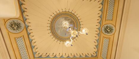 A ceiling with a central circular mirror surrounded by decorative elements and a chandelier.