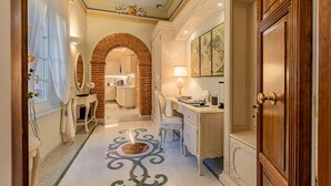 A hallway with a tiled floor, a desk with a lamp, a wooden door, and a framed map on the wall.