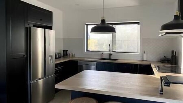 A modern kitchen with a central island, stainless steel appliances, and a window providing natural light. - New home Family Retreat near Pambula | 4bd 7guests (Broadwater)