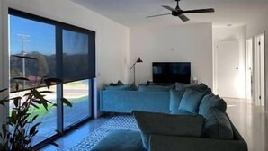 A modern living room with a large sliding glass door, a ceiling fan, and a flat-screen TV. - New home Family Retreat near Pambula | 4bd 7guests (Broadwater)