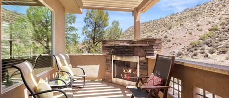 A covered patio with a stone fireplace, outdoor seating, and a view of a desert landscape.