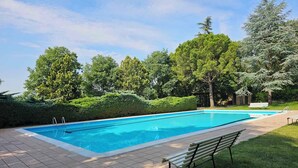 A rectangular swimming pool with a tiled deck, surrounded by well-maintained grass and trees. - Holiday apartment with air conditioning, swimming pool, tennis (Colà di Lazise)