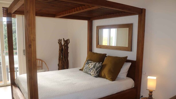 A four-poster bed with a white bedspread and two pillows, a wooden headboard, a small bedside table with a lamp, and a window with a wooden frame. - Holiday apartment with air conditioning, swimming pool, tennis (Colà di Lazise)