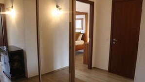 A hallway with a wooden floor, a dark wooden cabinet, and a door leading to a bedroom with a bed and a window. - Holiday apartment with air conditioning, swimming pool, tennis (Colà di Lazise)