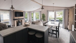 A modern kitchen with a central island, dining area, and a large window providing a view of the outdoors. - Shoreline - a spacious, well appointed lodge overlooking Christchurch Harbour. (Christchurch)