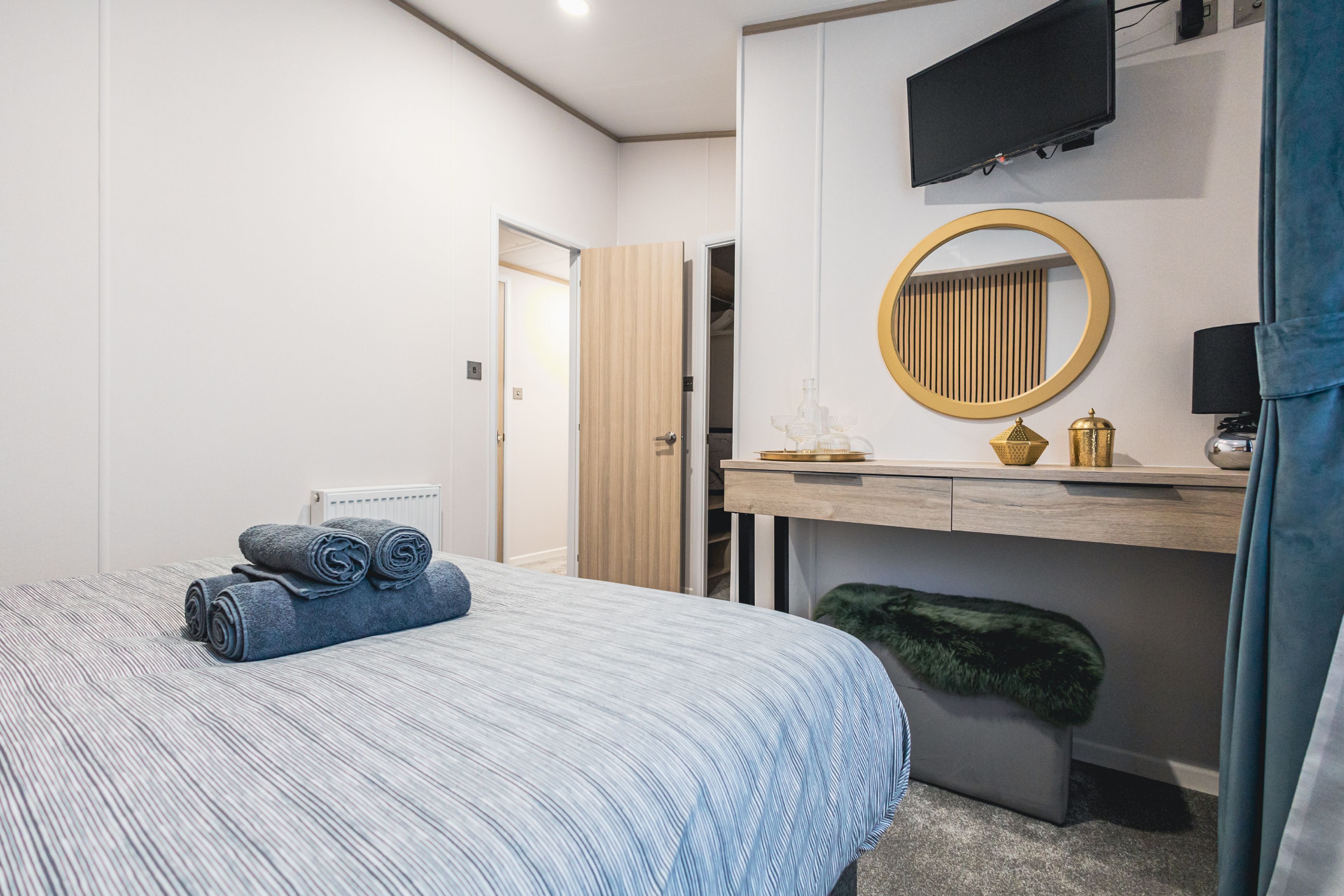 A modern bedroom with a bed, a desk, a mirror, and a television.