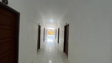 Un pasillo con paredes blancas y suelo de baldosas que conduce a una habitación luminosa con una pared amarilla.
