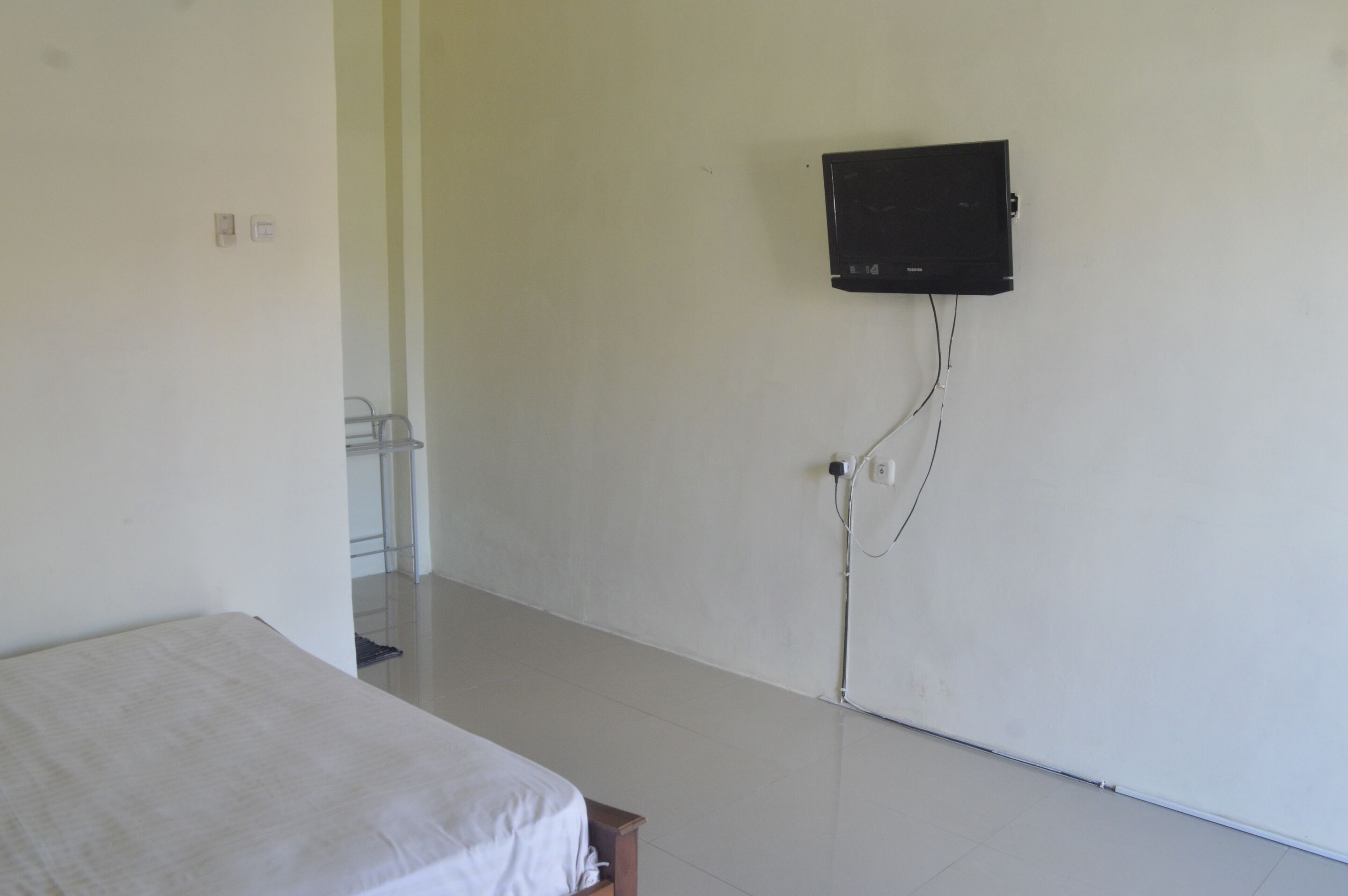 Una habitación con una cama, un televisor montado en la pared y un enchufe visible.