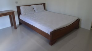 A single bed with a wooden frame and white bedding in a room with white walls and a tiled floor.