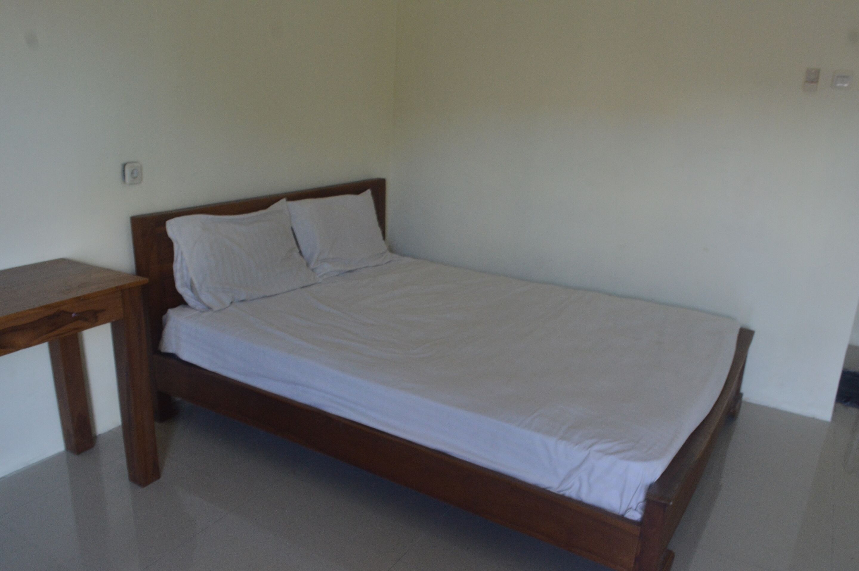 A single bed with a wooden frame and white bedding in a simple room with white walls and a wooden nightstand.