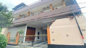 A multi-story residential building with a balcony on the upper floor, a gated entrance, and a small garden area.