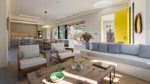A modern living room with a sofa, chairs, a coffee table, and a kitchen in the background. - Euphonia Residence by Athina Hospitality (Ermionida)