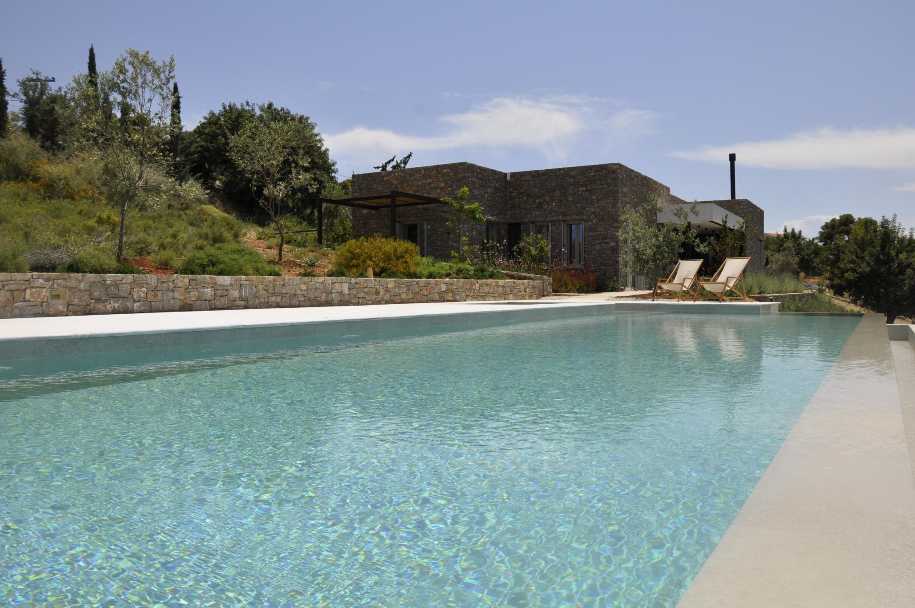 A modern house with a stone exterior, a swimming pool, and two lounge chairs by the pool.