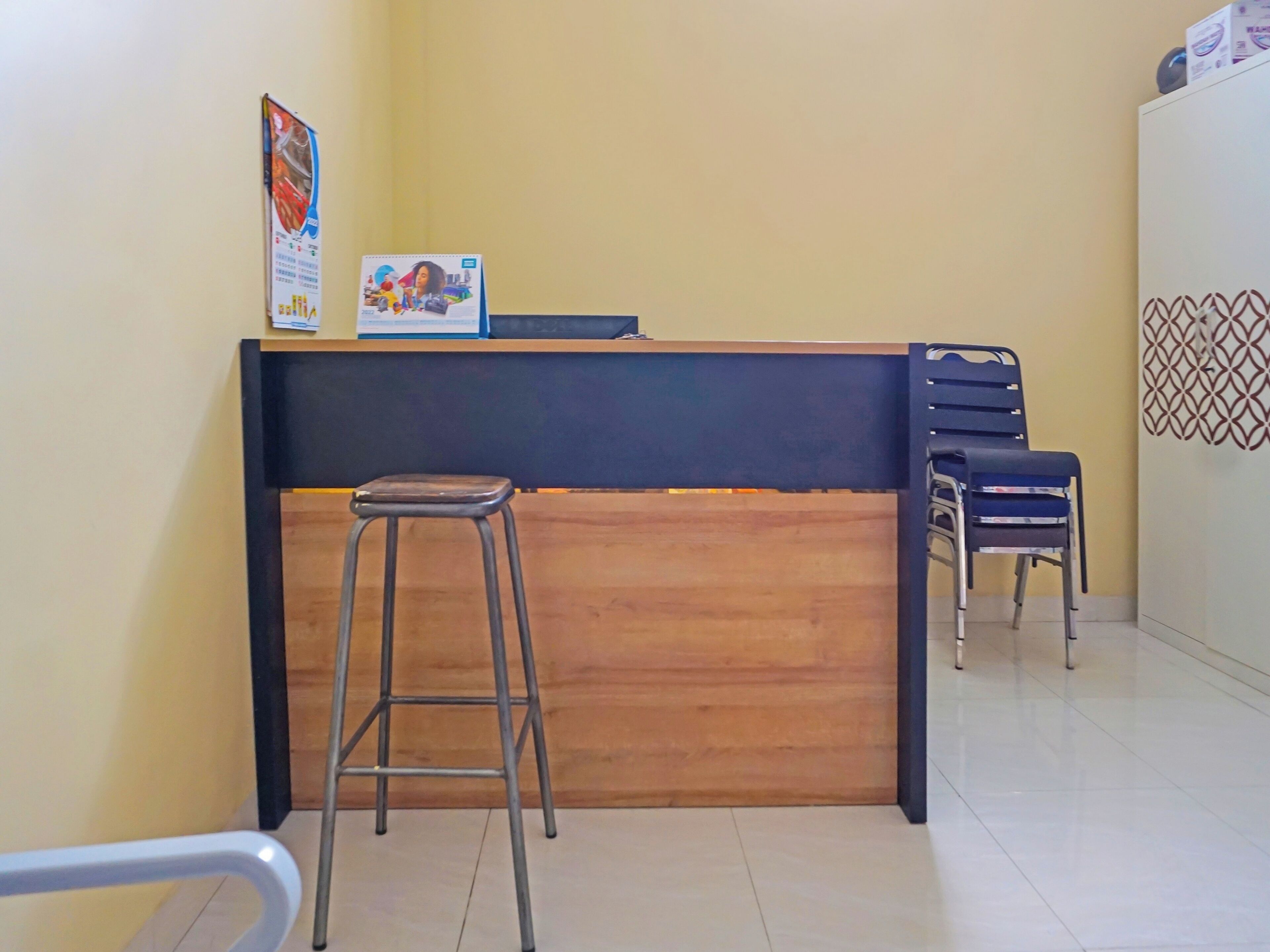 Un mostrador de recepción con encimera de madera y un taburete de metal, dos sillas azules y un adorno de pared con estampado.