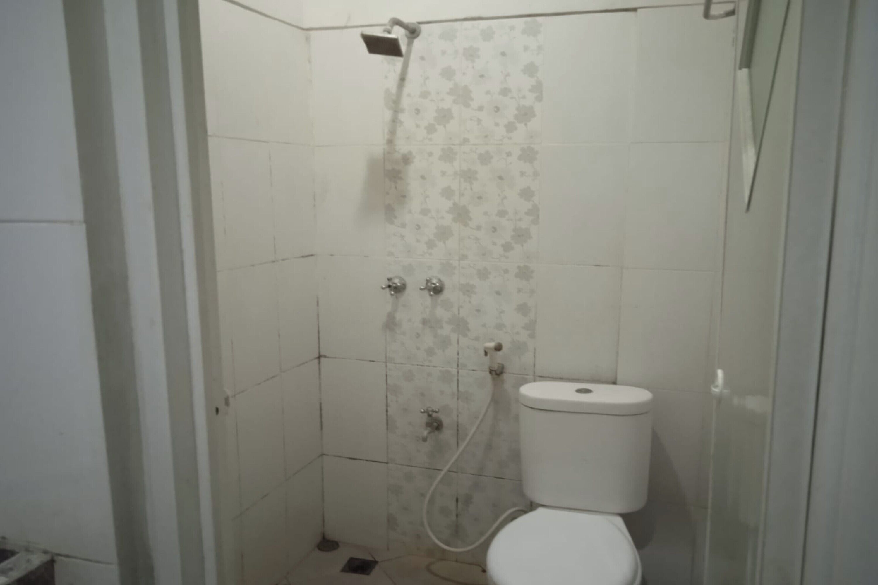 A small, enclosed shower area with a toilet, tiled walls, and a showerhead.