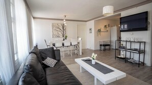 Una sala de estar moderna con un sofá de cuero negro, una mesa de centro blanca y una zona de comedor con sillas blancas.