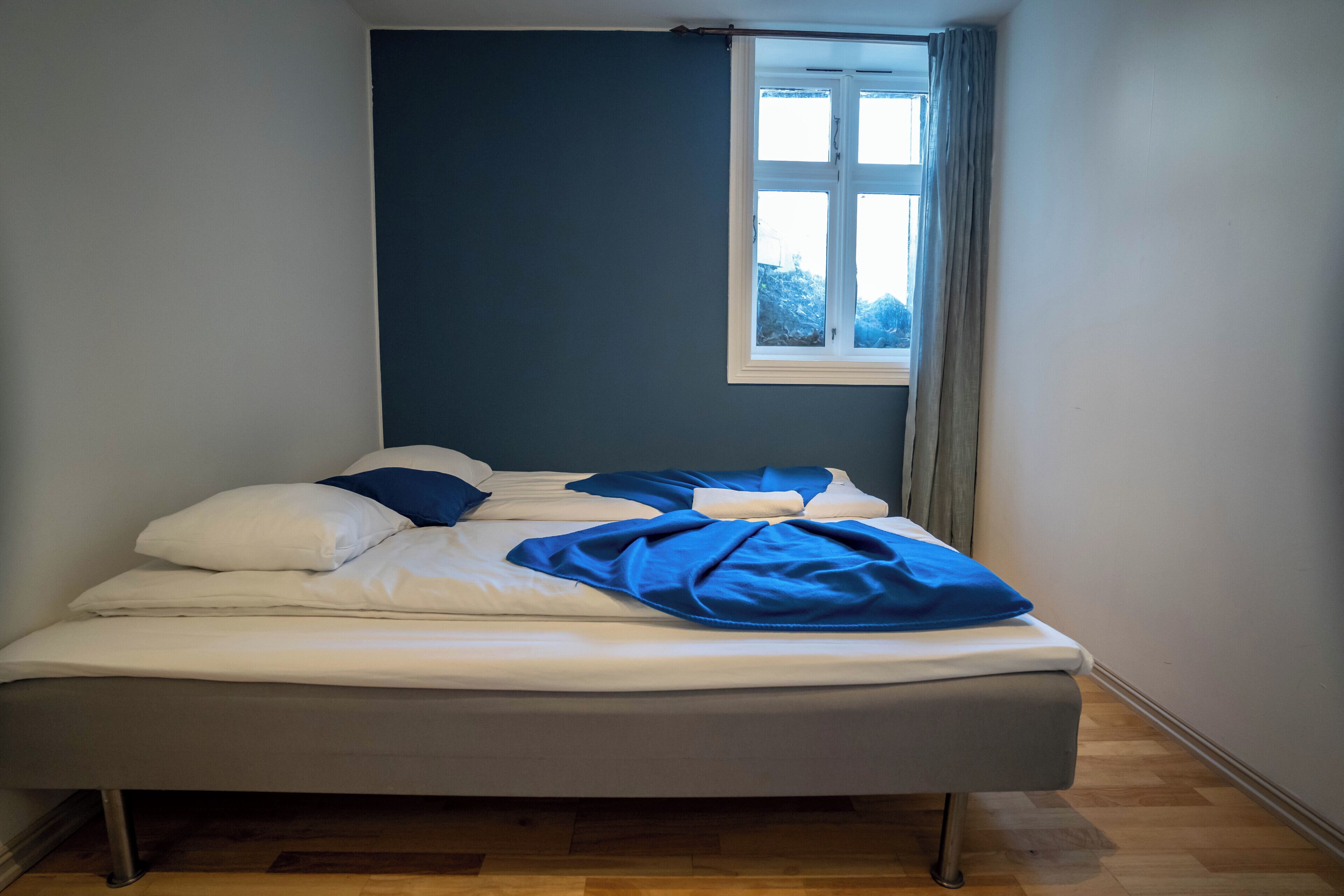 A single bed in a room with a window, wooden flooring, and a dark wall.