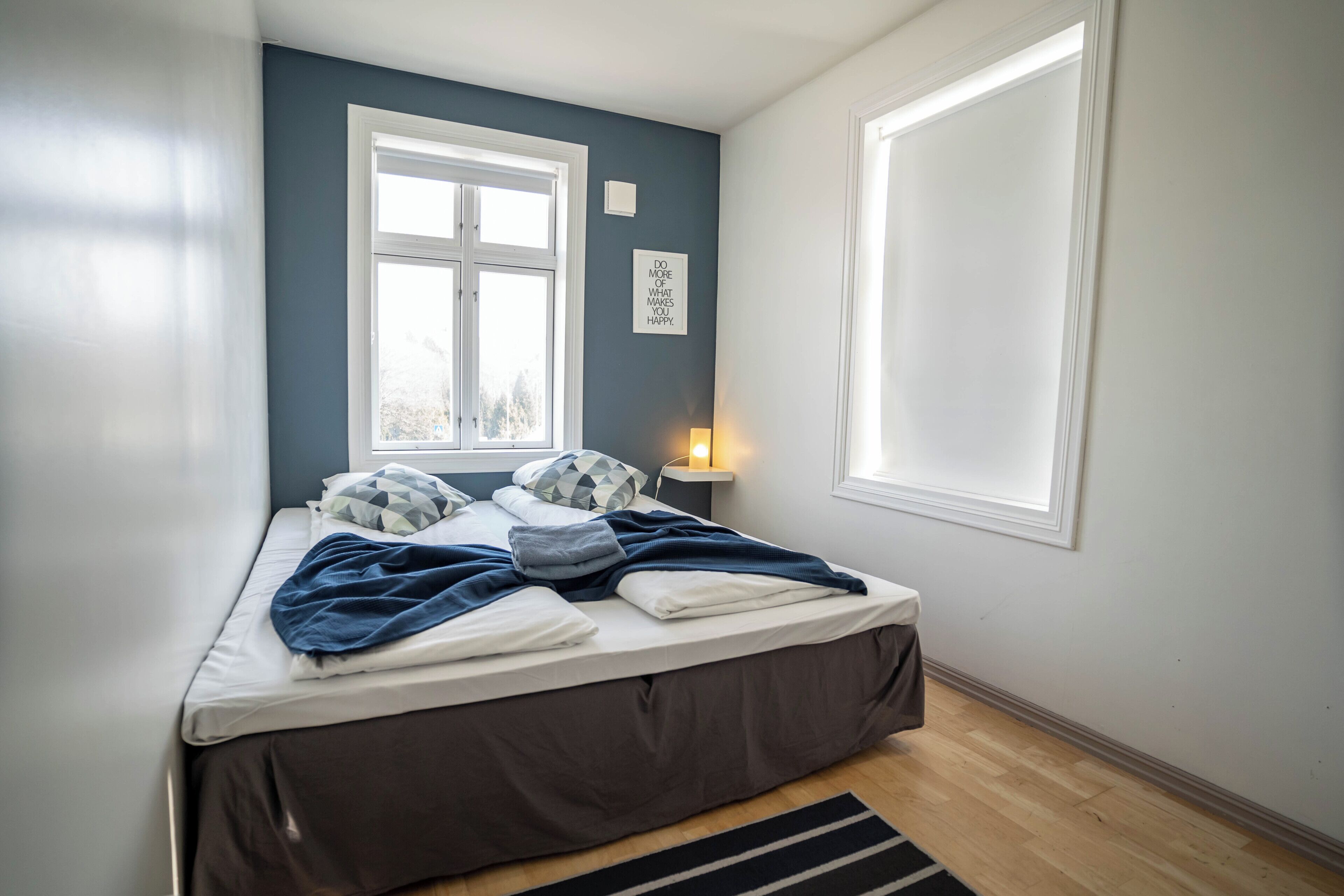 A bedroom with a bed, a window, a wall-mounted light, and a framed inspirational quote.